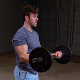 Man lifting 7.5lb black standard weight plates for strength training in a gym setting.
